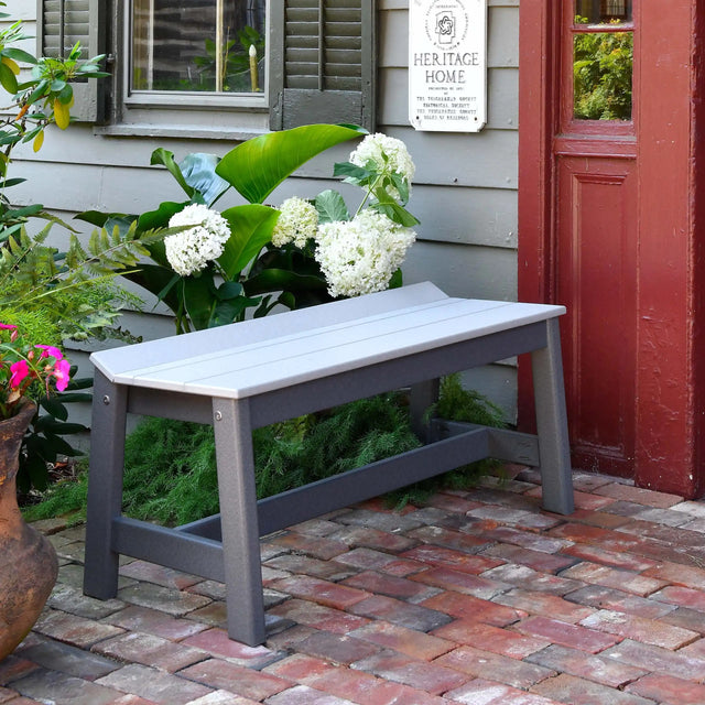 This is a lifestyle image showing the Dove Gray and Black colored dining bench on a red brick patio in front of a red door.