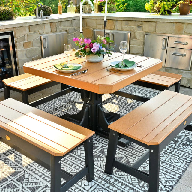 This is a lifestyle image showing the Cedar and Black colored square dining table surrounded by matching benches. The table is surrounded by a stone outdoor kitchen island.