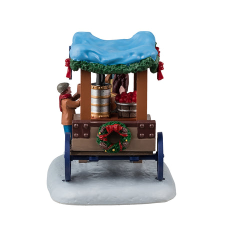 Resin table accent for a Lemax Village tabletop display. Designed to look like a wooden vendor cart. The sign reads "Coffee Wassail." The roof above the carriage is a light blue color and features a green garland around the edges. The vendor is wearing a marron jacket and top hat and is handing a cup to a young child wearing winter clothes. Inside the cart, there's a coffee maker and bowl of wassail warming over a heater. There's a decorated wreath on the back of the cart.