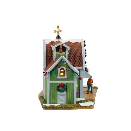 Resin lighted building for a Lemax display. Designed to look like a green barn turned into a petting zoo. There's a gold wind vine on the roof and multi-colored lights hanging on the roof. There are alpacas looking out the windows. Their names are Toby, Audrey and Phred. There are signs that read "Gifts," "Treats, Books, Squishes & More" and "Yarn Crafts." There are people feeding small goats behind a gray fence.