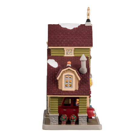 Porcelain lighted building for a Lemax display. Designed to look like a house turned into a drive-thru restaurant. There's a gold wind vine and snow on the roof. There are fall accents as well as wreaths and pine swag decorations. There's a red car ordering food in the drive thru. There's a boy sitting on a bale of hay next to a white dog. You can see a woman inside the building serving coffee.