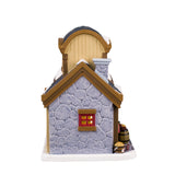 Porcelain lighted building for a Lemax Village display. Designed to look like a store booth connected to a building that is shaped like a coconut. There's snow on the roof and the sidewalk. There's a man behind the booth wearing an apron. On the upper level of the building, there's a Nut Butter Loft. There's a decorated wreath and garland near the front door. There are barrels of different nuts and a few squirrels.