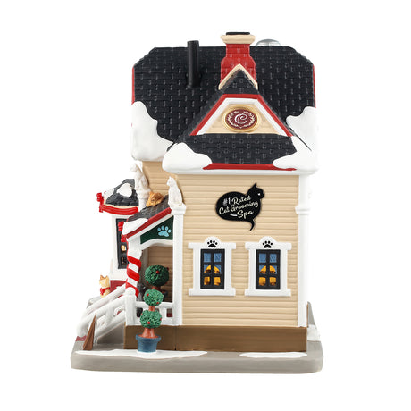 Porcelain lighted building for a Lemax display. Designed to look like a Victoria-era house that's been turned into a cat grooming office. There's snow on the roof and the sidewalk. There are different colored cats all over the place. Inside the window, you can see one of the groomers hard at work. There are red ribbon accents and two small potted trees.