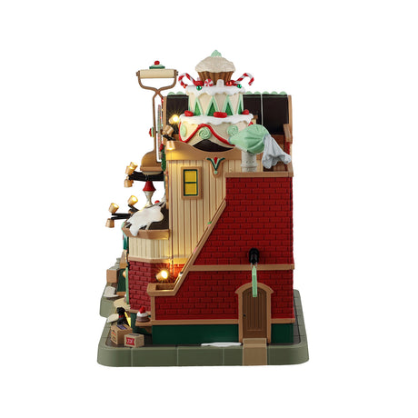 Resin lighted building for a Lemax display. Designed to look like an animated cake factory. A detailed, whimsical model of a "Christmas Cake Factory" with bright lights and animated figures depicting various festive baking activities. This resin lighted building captures the holiday spirit beautifully.