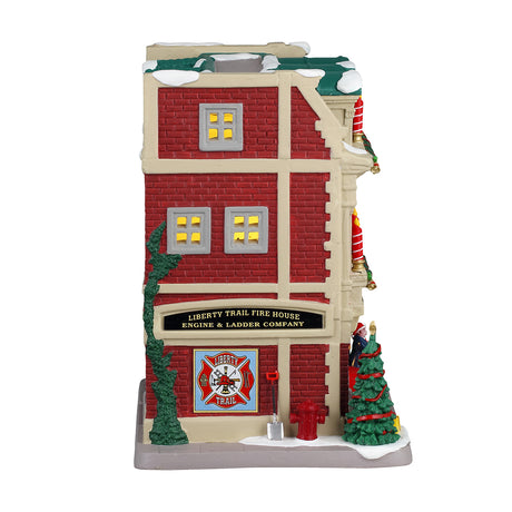 Porcelain lighted building for a Lemax display. Designed to look like a red brick fire house. There are large red and white striped candle accents, decorated wreaths and a Christmas tree. You can see the red firetruck in the garage and there's a lamppost next to the front door. There's snow on the roof and on the sidewalk.