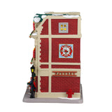 Porcelain lighted building for a Lemax display. Designed to look like a red brick fire house. There are large red and white striped candle accents, decorated wreaths and a Christmas tree. You can see the red firetruck in the garage and there's a lamppost next to the front door. There's snow on the roof and on the sidewalk.
