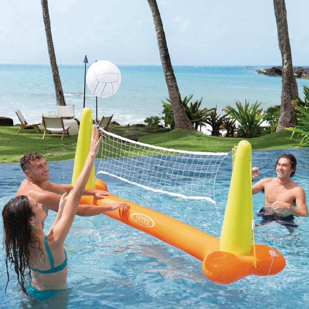 This is a lifestyle image showing three people using the inflatable volleyball net and inflatable volleyball in a pool near the beach.