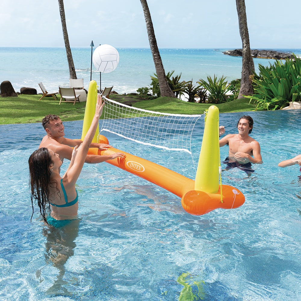 This is a lifestyle image showing three people using the inflatable volleyball net and inflatable volleyball in a pool near the beach.