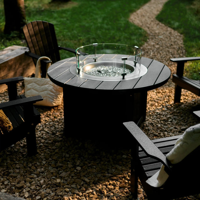 This is a lifestyle image showing the Black colored fire pit table surrounded by Black colored Adirondack chairs.