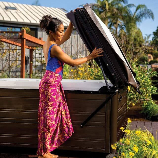 This image shows a woman using the UpRite lift system to lift the cover off of her Hot Springs hot tub.