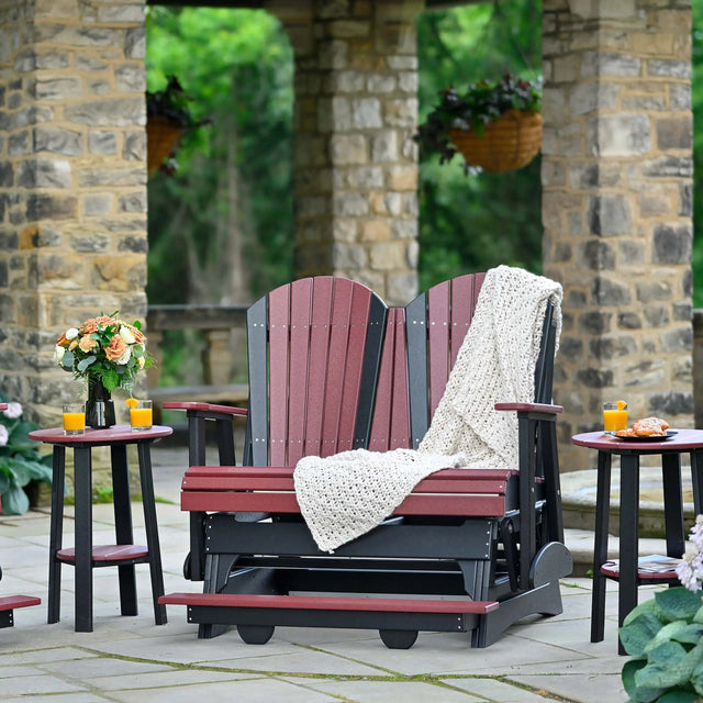 This is a lifestyle image showing the Cherrywood and Black colored Adirondack balcony glider on a stone patio.