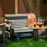 This is a lifestyle image of the Dove Gray and Black colored glider bench in a grassy yard. There's an orange and white colored blanket draped over the side.