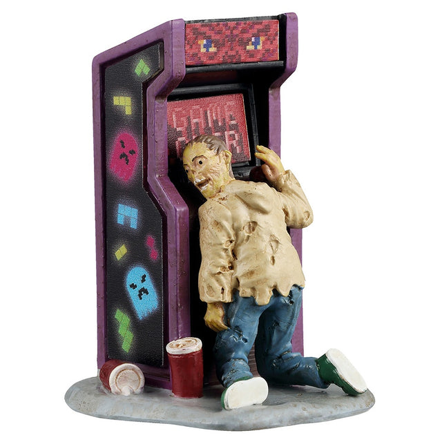 This image shows what this Lemax Spooky Town figurine looks like on a white background. It was designed to look like a zombie leaning up against a reto-looking arcade game. The screen reads "GAME OVER." There are two drinks discarded on the ground. The sides of the game are decorated with neon colored Tetris pieces and neon colored Pac-Man style ghosts.