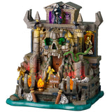 This image shows what this Lemax Spooky Town lighted building looks like on a white background. It was designed to look like a stone and brick cave shaped like a skull in some water. The front door is in the skull's mouth. There's a Grim Reaper standing up top. There are skulls and bones and fires and snakes.