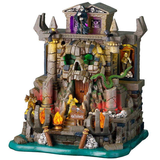 This image shows what this Lemax Spooky Town lighted building looks like on a white background. It was designed to look like a stone and brick cave shaped like a skull in some water. The front door is in the skull's mouth. There's a Grim Reaper standing up top. There are skulls and bones and fires and snakes.