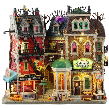 This image shows what this Lemax Spooky Town facade looks like on a white background. It's designed to look like a creepy, brick strip mall. There are jack-o-lantern accents and skulls with crossbones and small tombstones. There are also some fire escapes leading from the top to the bottom. 