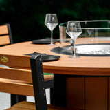 This is a lifestyle image showing the Cedar and Black colored fire table up close. There are plates and silverware and wine glasses on the table.