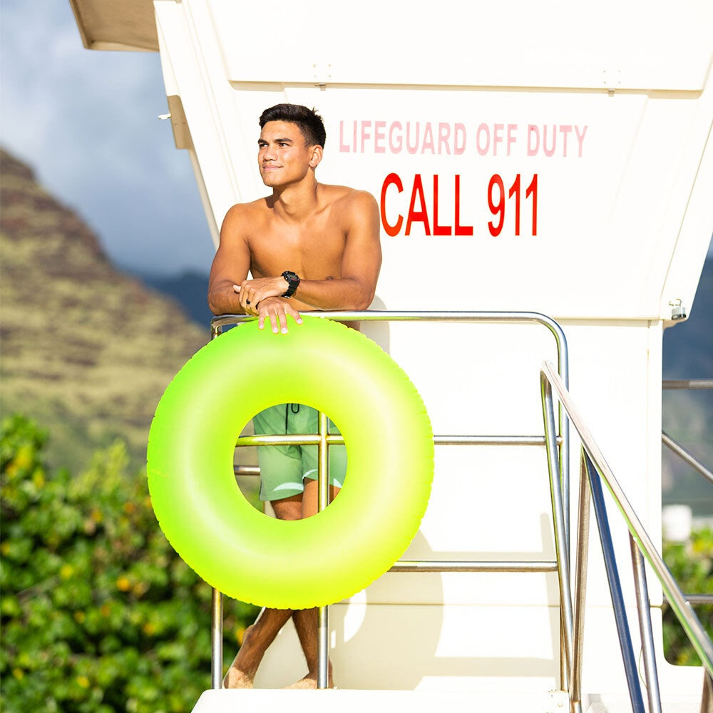This is a lifestyle image showing a man standing on a lifeguard station holding the neon yellow inner tube.