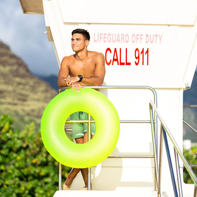 This is a lifestyle image showing a man standing on a lifeguard station holding the neon yellow inner tube.