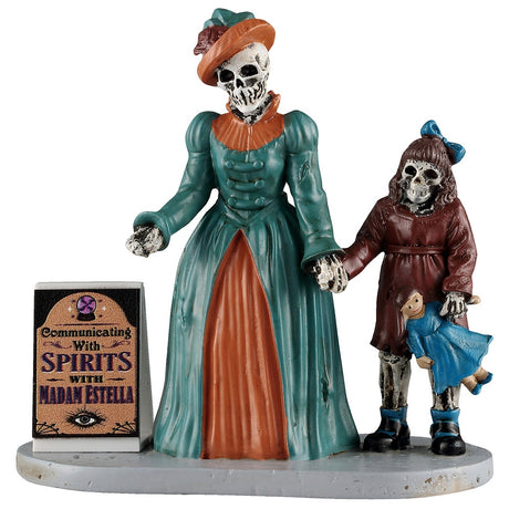 This image shows what this Lemax Spooky Town figurine looks like on a white background. It was designed to look like a skeletal woman wearing a burnt orange and teal colored Victorian-style dress and a matching hat. She is holding hands with a young skeletal girl wearing a brown dress with a blue bow in her hair. The little girl is holding onto a little dolly wearing a blue dress. They're standing next to a sign that reads "Communicating with Spirits with Madam Estella."