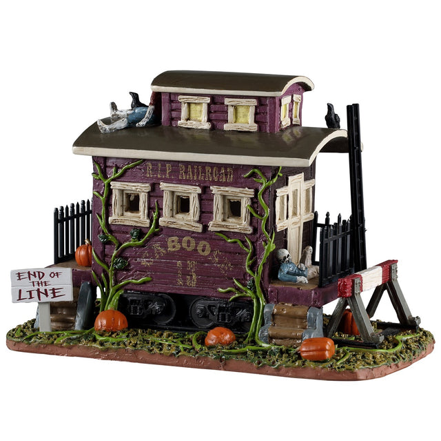 This image shows what this Spooky Town table accent looks like on a white background. It looks like the end of a rundown, very old train. There are crows on the roof and rotting pumpkins on the ground. There's a sign that reads "End of the Line."