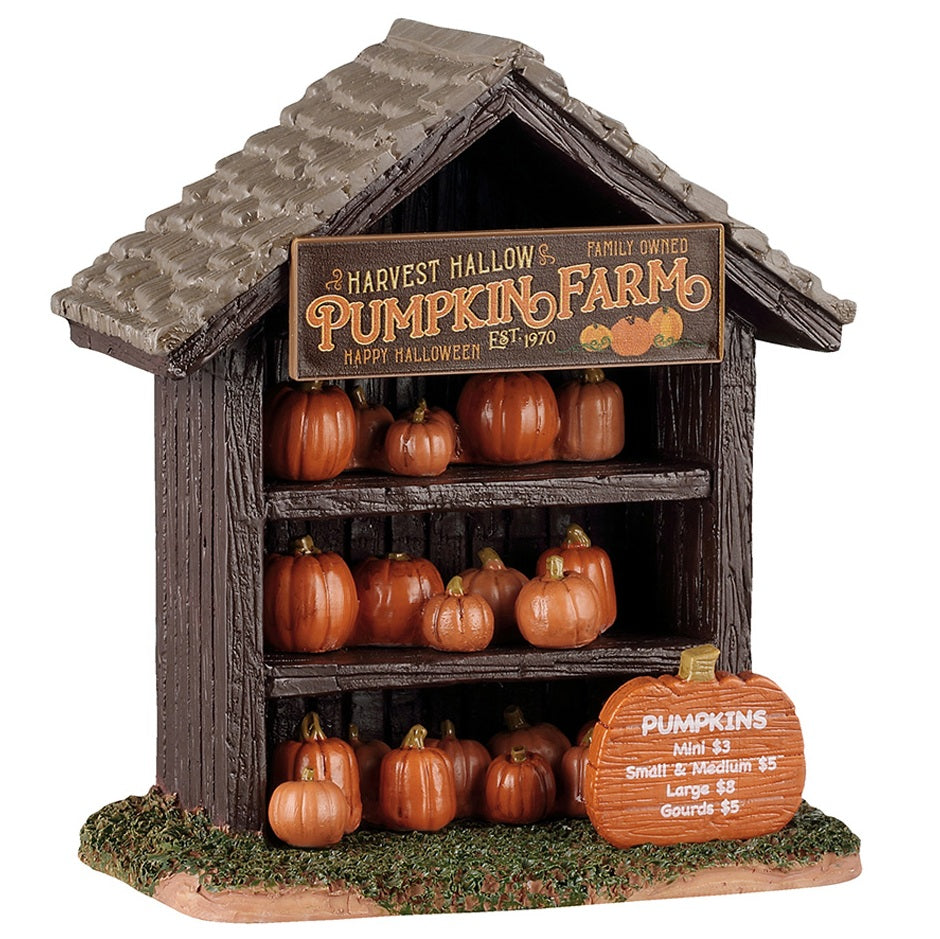This image shows what this Spooky Town table accent looks like on a white background. It was designed to look like a wooden stall with three shelves. There are different sized pumpkins on each shelf. There's a sign that reads "Harvest Hallow's Family Owned Pumpkin Farm. Established 1970. Happy Halloween!" There's also a pumpkin shaped sign in the grass that reads "Pumpkins: Mini $3. Small & Medium $5. Large $8. Gourds $5."