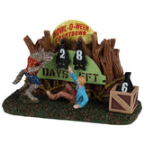 This image shows what this Spooky Town table accent looks like on a white background. The item is a countdown with numbers you can change, counting down to Halloween. There's a werewolf terrorizing a man who is scared on the ground. The moon is peaking out above the trees. The numbers are shaped like bats hanging upside down.