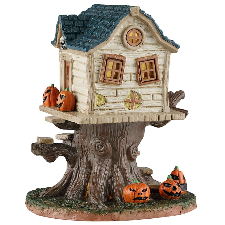 This image shows what this Lemax Spooky Town table accent looks like on a white background. It's designed to look like a pale yellow, semi-dilapidated tree house. It's decorated with jack-o-lanterns.
