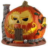 This image shows what this Lemax Spooky Town table accent looks like on a white background. It was designed to look like a house made out of a giant evil-looking jack-o-lantern with a brick chimney. The eyes and the mouth glow yellow. There's a skull on both sides of the front door.