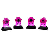 This image shows what these four Lemax Spooky Town accessories look like on a white background. They're designed to look like tombstones that light up with a pink light. The tombstones have a skull and crossbones on them and they read "R.I.P."