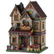 This image shows what this Lemax Spooky Town lighted building looks like on a white background. It was designed to look like a tall, old-timey home. Beautiful autumn arrangements of sunflowers and chrysanthemums perch below the porch while seasonal bales of hay and grinning jack-o’-lanterns line the way to the door. Beneath the awning, a colorful wreath entertains guests while they wait. Around the corner, fresh apple cider is available on the lawn.