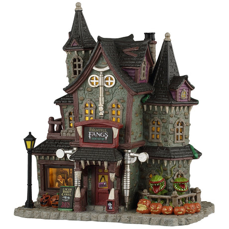 This image shows what this Lemax Spooky Town lighted building looks like on a white background. It was designed to look like a spooky, Victorian-era styled mansion. Above the front door, there's a sign that reads "Frightful Fangs Dentistry." There's also a sign off to the left of the front door that reads "Lycan Root Canal 30% off." There's a window in the front you can look into and see someone in the dentist's chair. Off to the right, there are plants with mouths and lots of jack-o-lanterns.