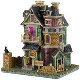 This image shows what this Lemax Spooky Town lighted building looks like on a white background. It was designed to look like an old-timey, dilapidated house. There's a monster standing on the balcony and another monster crawling out from the basement. There's a sign that reads "KEEP OUT," along with lots of boarded up windows and doors.