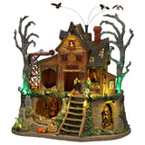 This image shows what this Lemax Sights and Sounds building looks like on a white background. It was designed to look like a dilapidated, wooden cabin with bare trees next to it. There are vultures circling above and monsters walking around. You can see the ground underneath the cabin. There's a skeleton in a cage, there are some tombstones and a creaky ladder.