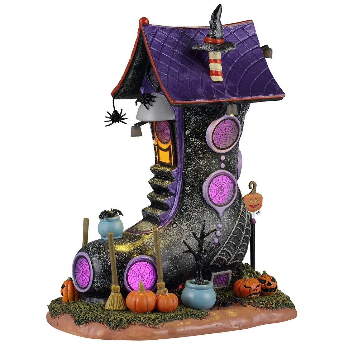 This image shows what this Lemax Spooky Town lighted building looks like on a white background. It was designed to look like a house made out of a black, glittery boot. It has lots of circular windows with spiderwebs on them. There are lots of brooms and jack-o-lanterns around the home.
