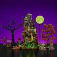 This image shows what this Lemax Spooky Town house set looks like on a purple background. It was designed to look like a very tall, dilapidated tree house. There are two trees: one bare and one has orange leaves. There's a scarecrow with a pumpkin head and two stacks of pumpkins. There are two trees with glowing eyes and a skeleton sitting in a rocking chair playing the guitar. There are skeletons and monsters walking up the treehouse steps. The moon is full and bright.