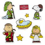 This image shows the Nativity scene Peanuts option. Linus, Charlie Brown and Snoopy are dressed like shepherds. Woodstock is in a manger, like baby Jesus. Sally is dressed as an angel. There are two yellow stars and a red sign that reads "The Christmas Play" in white font. 