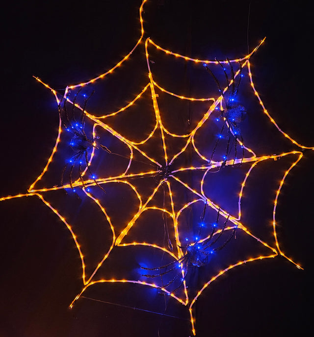This image shows a pre-lit spider web decoration with pre-lit spiders in it. The web is made of orange lights and the spiders are made of blue/purple lights.