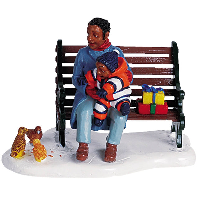 Polyresin figurine for a Lemax display. Designed to look like a mom and young child sitting on a wooden bench feeding birds. They're both wearing winter clothes and there's a wrapped gift next to them on the bench.