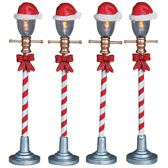 Village accents for a Lemax display. Designed to look like four lampposts. The poles look like red and white candy canes and there are Santa hats on top of the bulbs. Each lamp has a red bow tied to it.