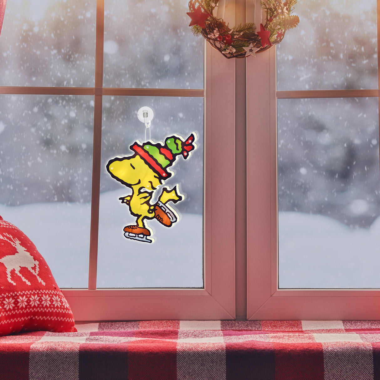 This is a lifestyle image showing the Woodstock decoration hanging in a window while it snows outside.