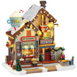 This image shows what this Lemax building looks like on a white background. It was designed to look like a tall building that sells drinks and food. The roof and sidewalk have snow on them. The roofline is decorated with lights. There are large fake mugs all over. There are signs that read "The Cocoa Shanty," "Hot Beverages!," "Snacks & Candy," "Welcome" and "Fireside Seating Inside!"