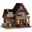 This image shows what this Lemax building looks like on a white background. It was designed to look like a red cottage turned into a gas station / post office. There are signs that read "Parker's Provisions, Gas, Post Office," "Parker's Corner," "Parker's Gas, Provisions, Snacks," "Cold Beer" and "Gas - Pay Inside!" There are gas pumps, freezers and a newspaper vending machine.