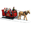 This image shows what this Lemax table accent looks like on a white background. It was designed to look like a horse pulling a sleigh full of people through the snow. The side of the sleigh reads "Pine Mountain Farm Caroling Sleigh Ride." The people in the sleigh are all wearing winter clothes and holding song books.