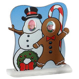 This image shows the face-in-hole board with the two kids standing behind it. The board is designed to look like a snowman wearing a black top hat and a gingerbread cookie wearing a red bow tie. The girl has her face in the place of the snowman's face. The boy has his face in the place of the gingerbread cookie.