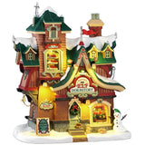 This image shows what this Lemax building looks like on a white background. It was designed to look like a dormitory for Santa's elves. The roofs and the sidewalk are covered in snow. Someone made a snowman on the corner and there are some wild animals standing near it. There's a window near the top of the building where you can see sets of bunk beds with elves sleeping.