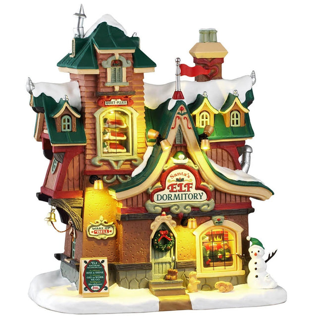 This image shows what this Lemax building looks like on a white background. It was designed to look like a dormitory for Santa's elves. The roofs and the sidewalk are covered in snow. Someone made a snowman on the corner and there are some wild animals standing near it. There's a window near the top of the building where you can see sets of bunk beds with elves sleeping.