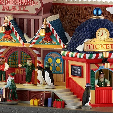 This is an up close view of the lighted building. There are presents and suitcases on the sidewalk and lots of elves working.