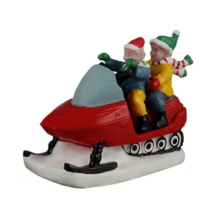 This image shows two elves riding a red snowmobile. The front elf is wearing a red Santa hat, green gloves, a blue jacket, yellow pants and black shoes. The back elf is wearing a green Santa hat, red gloves, a red/green/white striped scarf, a yellow jacket, blue pants and black shoes.