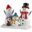 This image shows what this Lemax Santa's Wonderland figurine looks like on a white background. It was designed to look like two tall snow people and one small snow person. The tall one on the left is wearing a red knit hat and a white and purple striped scarf. The tall one on the right is wearing a black and red top hat and a red scarf. The small one is wearing a blue knit hat and a yellow scarf. There's also a brown bunny standing with them.